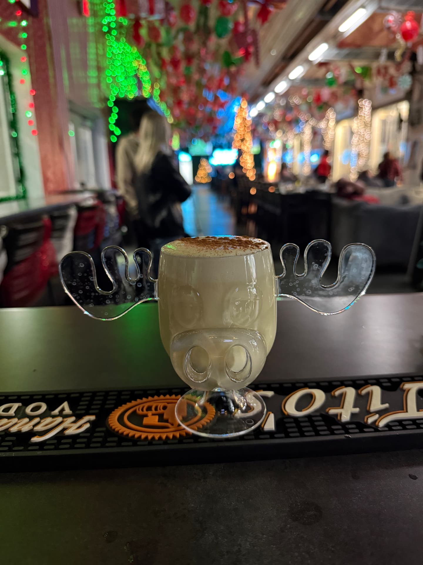 Holiday eggnog cocktail in a moose mug on the bar with Christmas lights behind