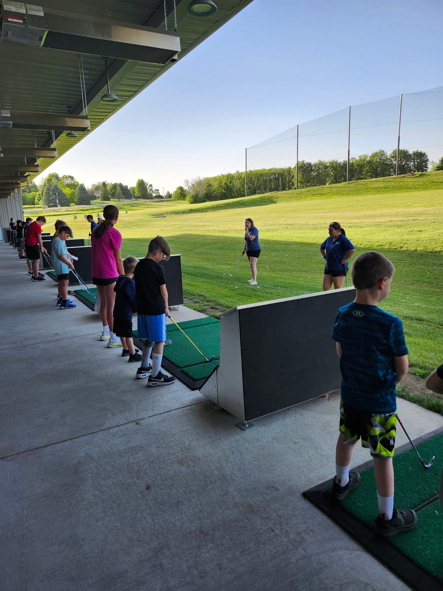 Junior golfers lined up at the Flight Zone outdoor bays during a clinic